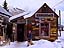 Resident Tracy Foster and loyal friend smile for the camera in front local landmark, Camp 4 coffee, with snowy Crested Butte summit in the background. The season is upon us for winter fun!